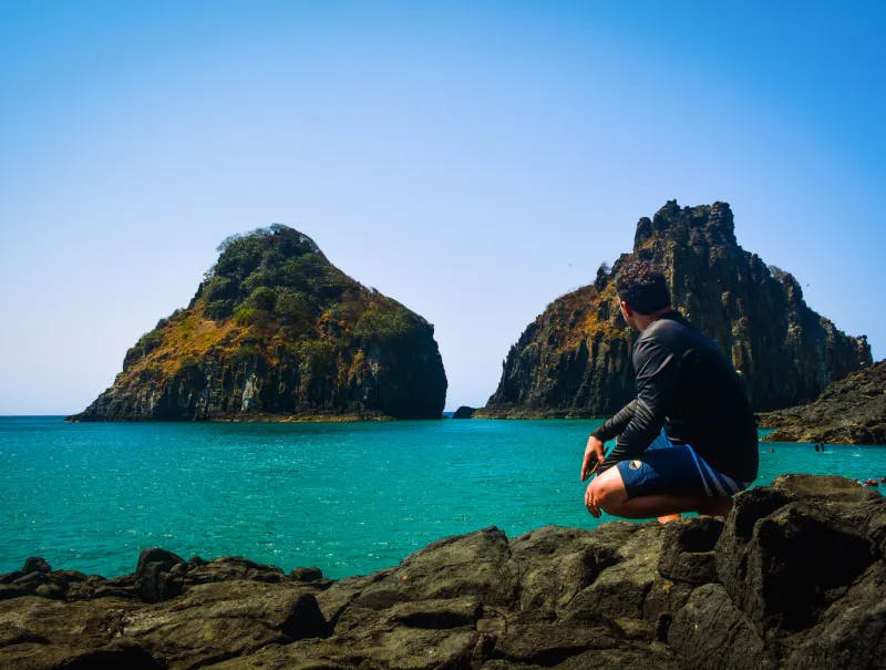 Man squatting on a rocky coast looking at a beautiful cove of water
