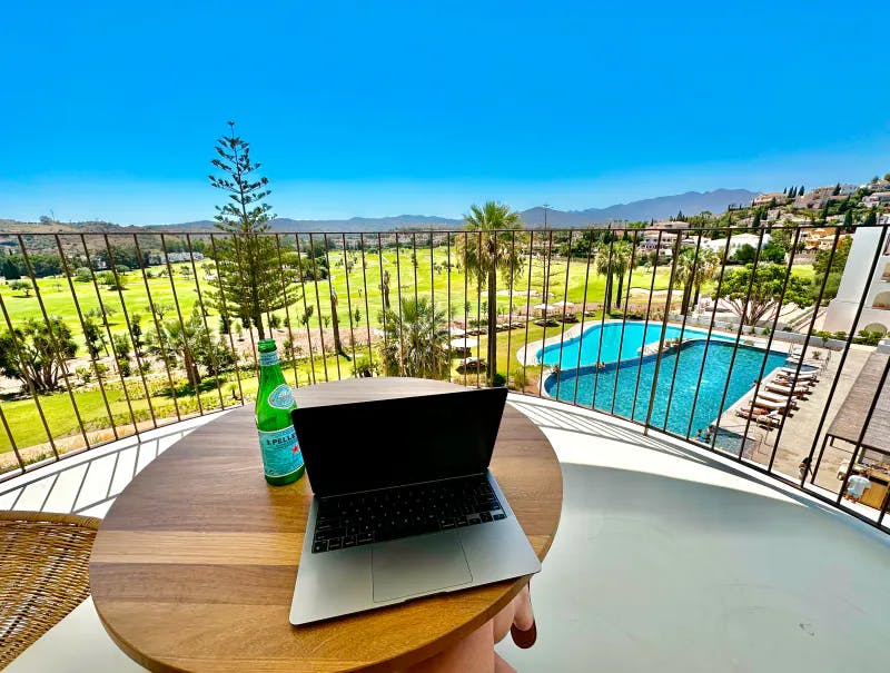 A laptop and bottle of water sitting on a table overlooking a view of a resort with mountains and a pool