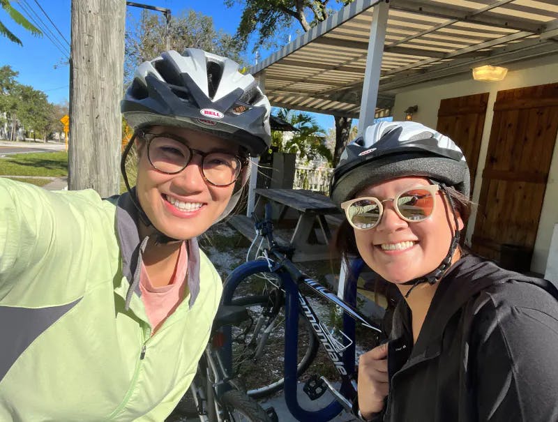 Two women smiling in a selfie with bike helmets on
