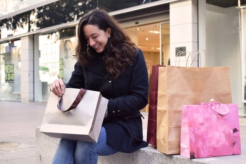 Woman sitting outside a retail store, looking in her bags and smiling, representing personalized shopping experience